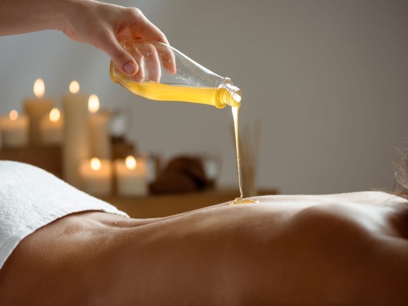 Honey pouring on girl's naked back in spa salon. Copy space.